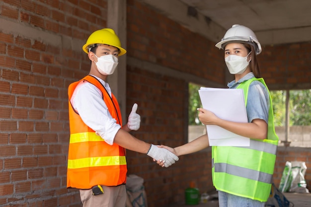 Concepto de ingeniero El trabajador de ingeniería masculino que usa uniforme naranja estrechando la mano con la trabajadora que usa uniforme verde