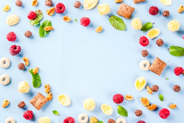 Concepto de ingredientes de desayuno saludable. Varios cereales para el desayuno, frambuesas y menta sobre fondo azul, marco de vista superior de espacio de copia