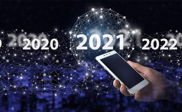 Concepto Inicio Año Nuevo 2021 Asimiento de la mano smartphone blanco con holograma digital 2021 ciudad icono oscuro fondo borroso. Bienvenido año 2021 concepto de tarjeta de año nuevo empresarial