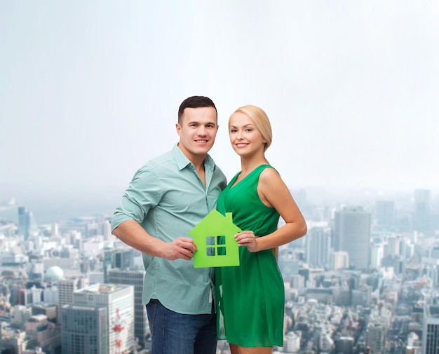 concepto inmobiliario, familiar y de pareja - pareja sonriente sosteniendo una casa de papel verde