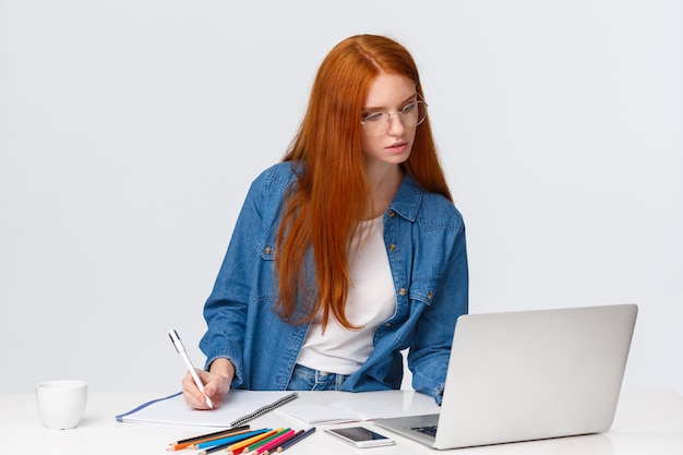 Concepto de inspiración, trabajo y arte. Mujer pelirroja linda ocupada enfocada en gafas