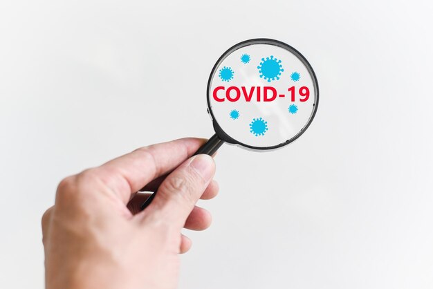 Concepto de investigación y tratamiento de COVID-19 La mano del médico sostiene una lupa para buscar la vacuna Coronavirus el virus COVID-19