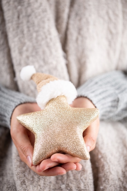 Concepto de invierno manos jóvenes sosteniendo la decoración de navidad. idea de decoración navideña. decoración navideña en manos de una mujer, fondo con bokeh dorado.