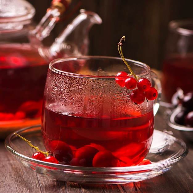 Concepto del invierno o del otoño: té rojo caliente de la baya con las pasas rojas y la cereza en la tabla marrón rústica.