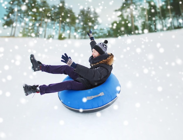 concepto de invierno, ocio, deporte y personas - adolescente feliz o joven deslizándose por el tubo de nieve