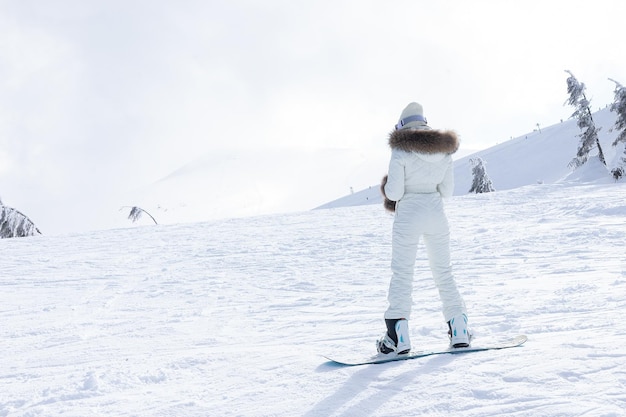 Concepto de invierno, ocio, deporte y personas: una chica en una tabla de snowboard baja por la ladera de la montaña
