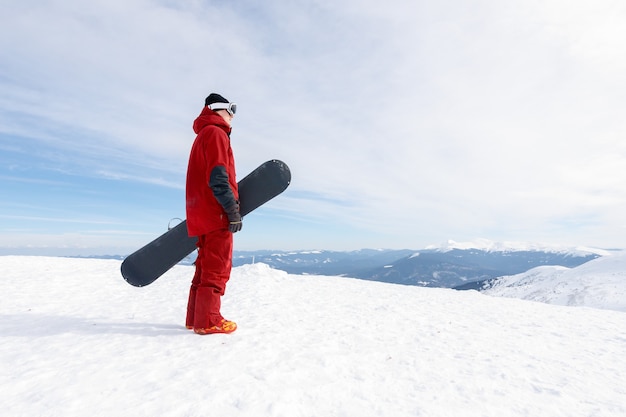 Concepto de invierno, ocio, deporte y personas: el snowboarder se encuentra en una pendiente de travesía y sostiene la tabla de snowboard. Concepto de esquí