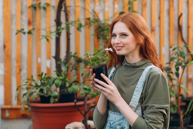 Concepto de jardinería doméstica. Mujer bonita joven que huele la flor en maceta. Primavera.