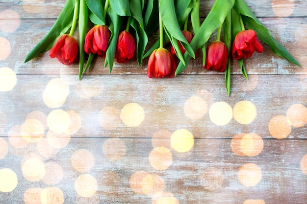 concepto de jardinería, flores, publicidad y vacaciones - cierre de tulipanes rojos sobre fondo de madera sobre luces