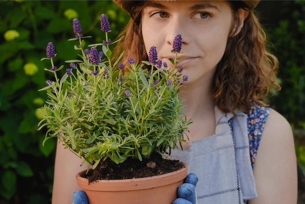 Concepto de jardinería Mujer joven jardinero sostiene planta de lavanda en maceta al aire libre
