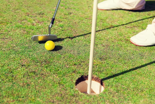 concepto de juego, entretenimiento, deporte, gente y ocio - cerca del hombre jugando al golf y poniendo la pelota con el palo de metal en el hoyo en el campo de golf