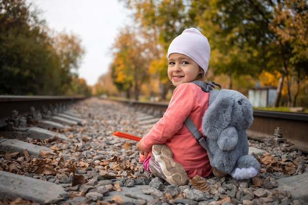 concepto de juegos de niños peligrosos. chica alegre se sienta solo en las vías del tren.