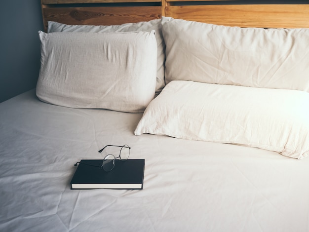 Foto concepto de lectura y relax anteojos y libro negro en la cama de madera del desván en dormitorio.