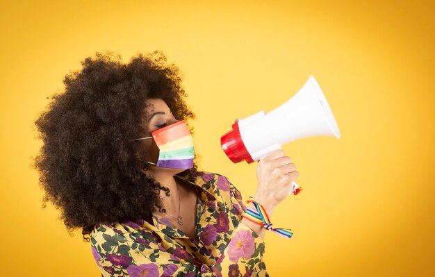 Concepto lgbtq. Chica caucásica positiva con pelo rizado afro sosteniendo la bandera del arco iris aislado en estudio