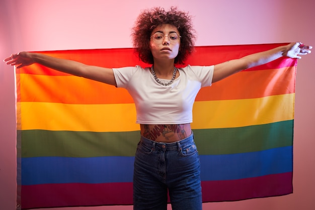 Concepto lgbtq. Chica caucásica positiva con pelo rizado afro sosteniendo la bandera del arco iris aislado