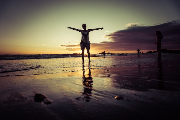 Foto concepto de libertad. silueta chica con los brazos abiertos caminando en la playa de arena durante la puesta de sol. reflexiones