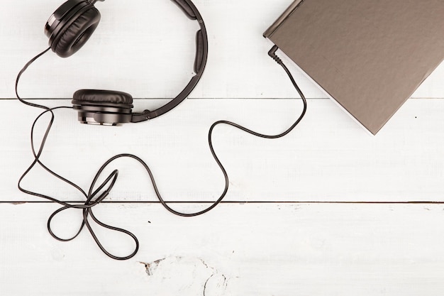 Foto concepto de libro de audio con libro negro y auriculares en madera blanca