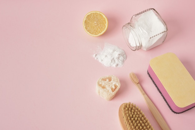 Concepto de limpieza ecológico guantes esponja de madera limón y soda sobre fondo rosa