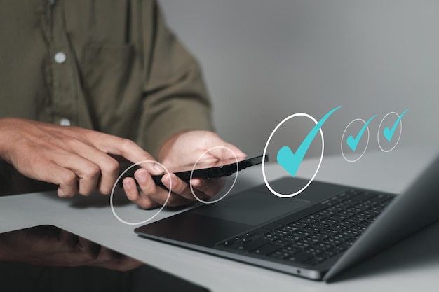Concepto de lista de comprobación Hombre que utiliza un teléfono inteligente y una computadora portátil para marcar la lista de control y realiza una prueba de encuesta de evaluación en línea para aprobar el proyecto de negocio Garantía de calidad y garantía ISO