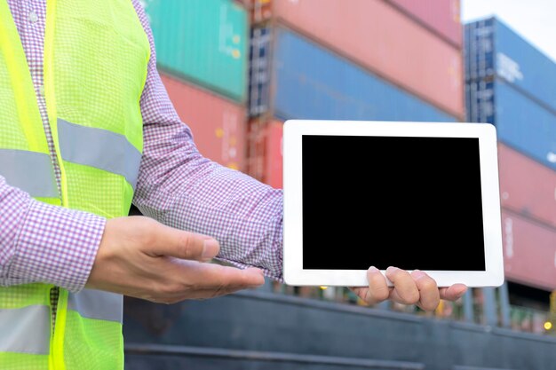 Concepto logístico La ingeniería sostiene una tableta Espacio libre para poder ingresar texto o imágenes para crear un medio publicitario El fondo es un gran contenedor de transporte de carga