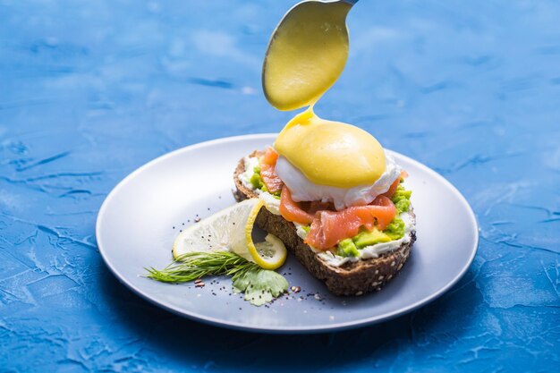 Concepto de mañana y desayuno: preparación de sándwich con salmón, cuchara se vierte salsa.