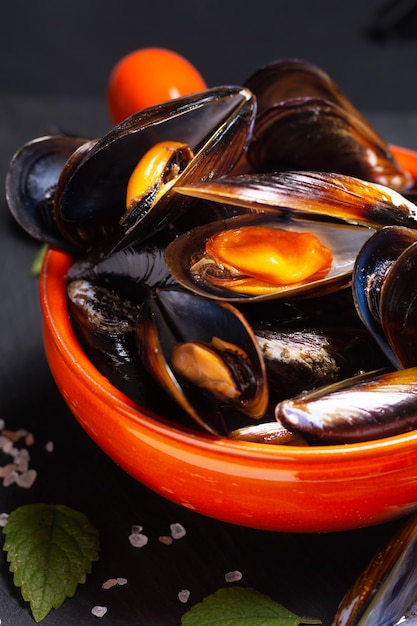 Concepto de mariscos mejillones en recipiente de mango naranja sobre piedra pizarra negra con espacio de copia