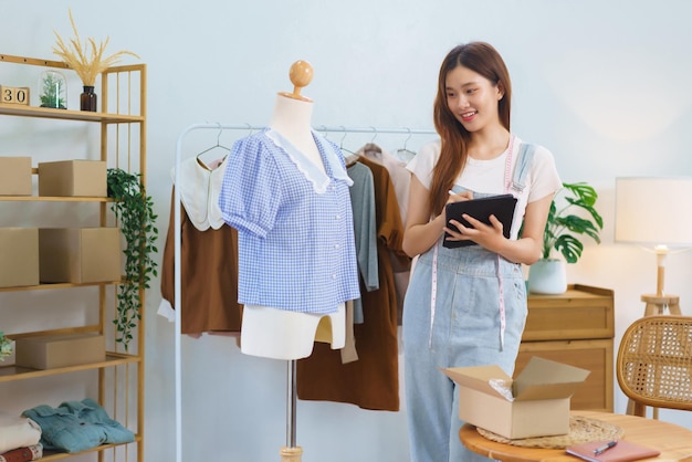 Concepto de marketing en línea Mujeres asiáticas que venden ropa en transmisión de video y verifican pedidos en tableta