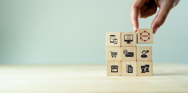 Concepto de marketing omnicanal Mercadeo en línea digital venta de comercio Para el compromiso del cliente por canales integrados en línea y fuera de línea La mano sostiene un cubo de madera con texto omni de pie con icono omni
