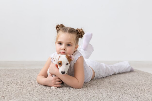 Concepto de mascotas, infancia y animales - Niña pequeña jugando en el suelo con el cachorro Jack Russell Terrier