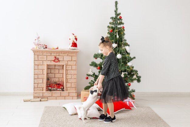 Concepto de mascotas, vacaciones y Navidad - Niña jugando con el cachorro Jack Russell Terrier cerca del árbol de Navidad.