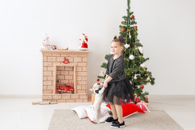 Concepto de mascotas, vacaciones y Navidad - Niña jugando con el cachorro Jack Russell Terrier cerca del árbol de Navidad.