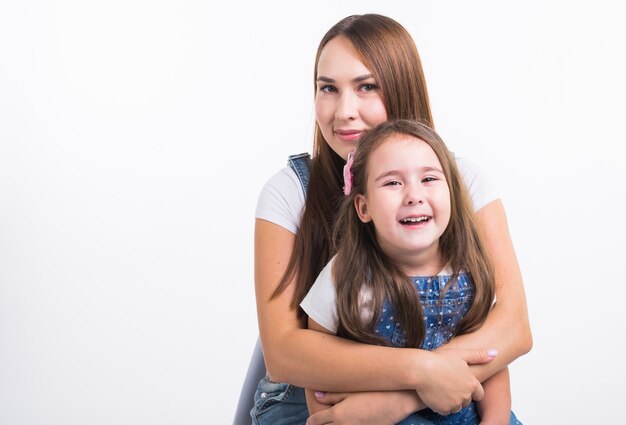 Concepto de maternidad, familia y relación: madre feliz e hija pequeña divirtiéndose en la pared blanca.