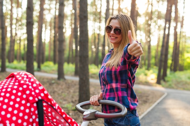 Concepto de maternidad feliz - mujer con cochecito mostrando los pulgares para arriba al aire libre.