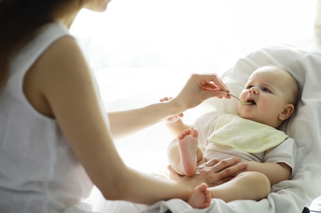 Concepto de maternidad. Una joven madre alimenta a su pequeño bebé. Primer señuelo y lactancia. Familia numerosa vestida de blanco.