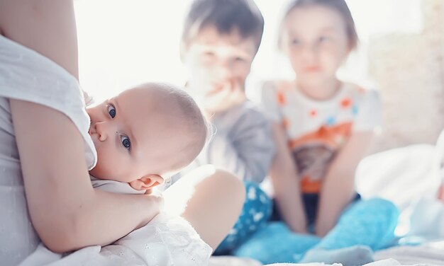 Concepto de maternidad. Una joven madre alimenta a su pequeño bebé. Primer señuelo y lactancia. Familia numerosa vestida de blanco.