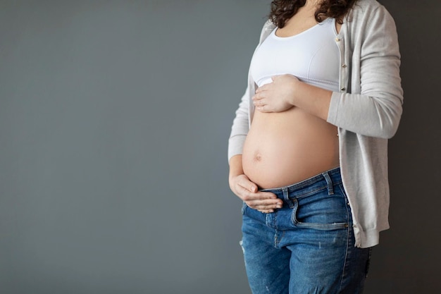 Concepto de maternidad tiro recortado de joven embarazada abrazando el vientre con las manos
