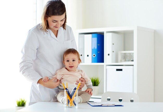 concepto de medicina, atención médica, pediatría y personas - médico o pediatra feliz sosteniendo al bebé en un examen médico en la clínica