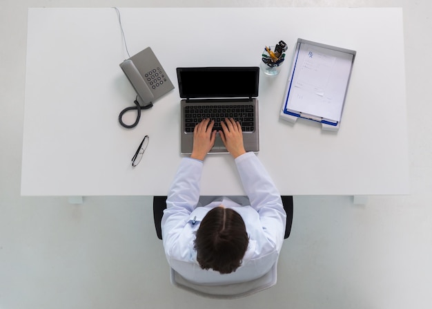 Foto concepto de medicina, atención médica y personas - médico con receta escribiendo computadora portátil sentado en la mesa en la clínica