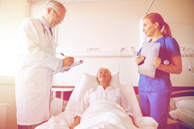 concepto de medicina, edad, atención médica y personas - médico y enfermera con cuadernos visitando a una paciente anciana en la sala del hospital