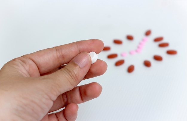 Concepto de medicina; Mano sostiene una medicina blanca con fondo blanco y reloj de pastillas.