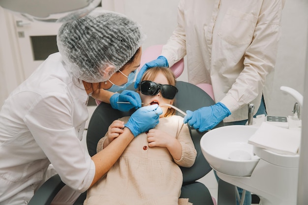 Concepto de medicina, odontología y salud. Un dentista con un taladro dental y un eyector de saliva trata los dientes de un niño en una clínica dental.