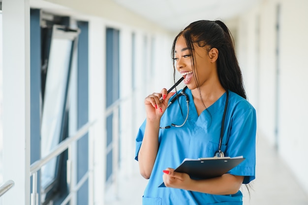 Concepto de medicina, profesión y cuidado de la salud - feliz sonriente doctora afroamericana con estetoscopio sobre fondo de hospital