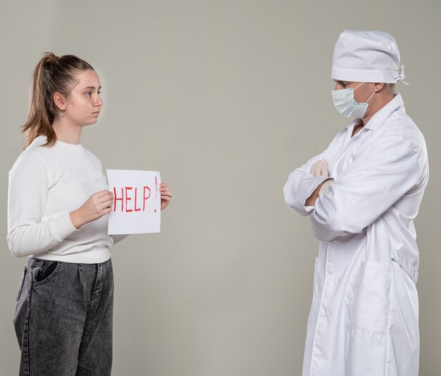 Concepto médico y sanitario. Jovencita pidiendo ayuda a un médico sobre pared gris