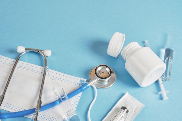 Concepto médico de tiempo de salud. Pastillas mascarilla ampolla jeringa con estetoscopio sobre un fondo azul copia espacio vista superior