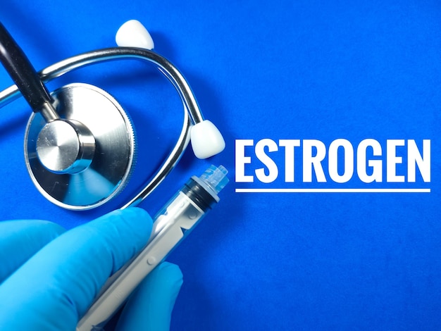 Concepto médicoTexto ESTROGEN con la mano usando guantes de nitrilojeringa y estetoscopio sobre fondo azul