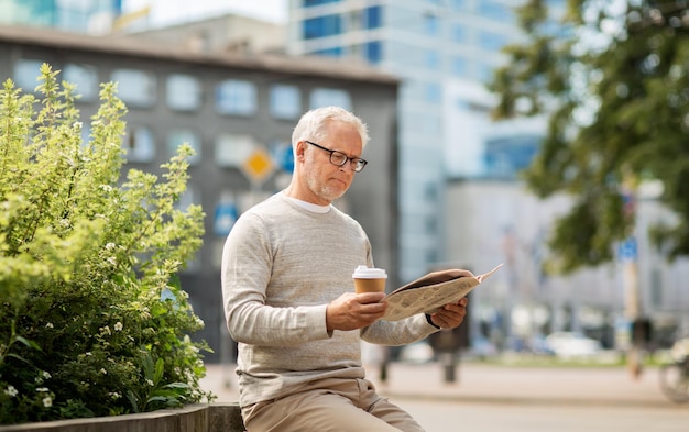 concepto de medios de comunicación, noticias y personas - hombre mayor leyendo el periódico y bebiendo café en la ciudad