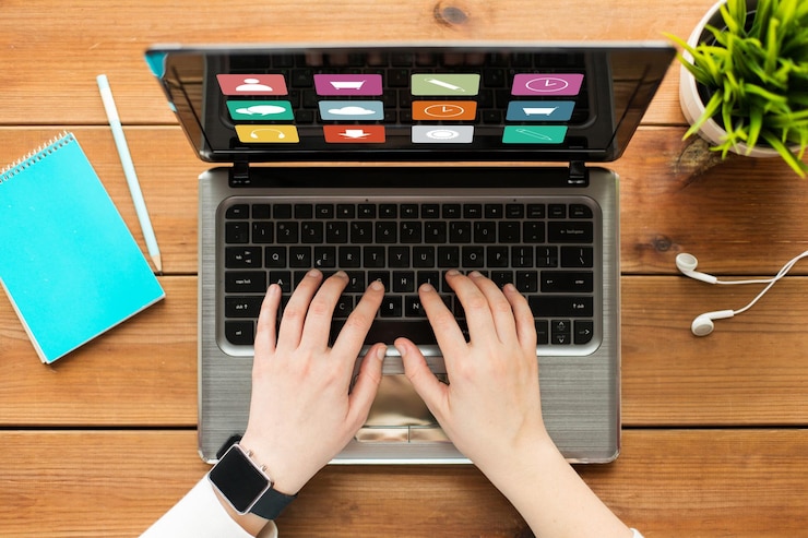 Foto concepto de medios, negocios, personas y tecnología: cierre de una mujer o estudiante escribiendo en una computadora portátil con íconos de menú en pantalla, cuaderno y auriculares en una mesa de madera