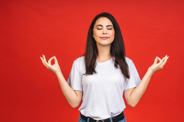 El concepto de meditación Una hermosa joven se encuentra en una pose meditativa disfruta de un ambiente tranquilo sostiene sus manos en un gesto de oración aislado sobre fondo rojo