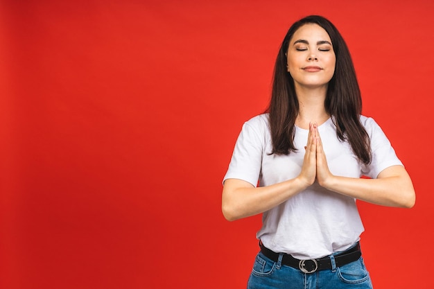 El concepto de meditación Una hermosa joven se encuentra en una pose meditativa disfruta de un ambiente tranquilo sostiene sus manos en un gesto de oración aislado sobre fondo rojo