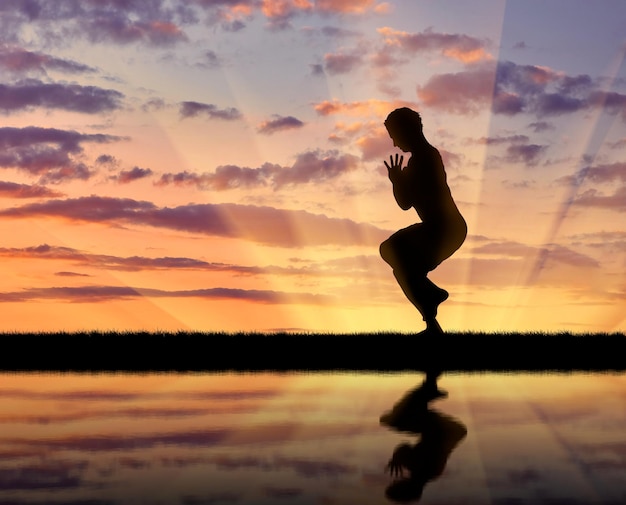 Concepto de meditación y relajación. Silueta de un hombre practicando yoga al atardecer y reflejo en el agua